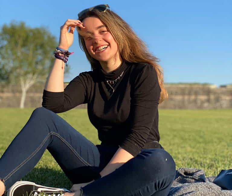 Una estudiante de Medicina sonríe. Está sentada sobre el césped de la Ciudadela en Pamplona.